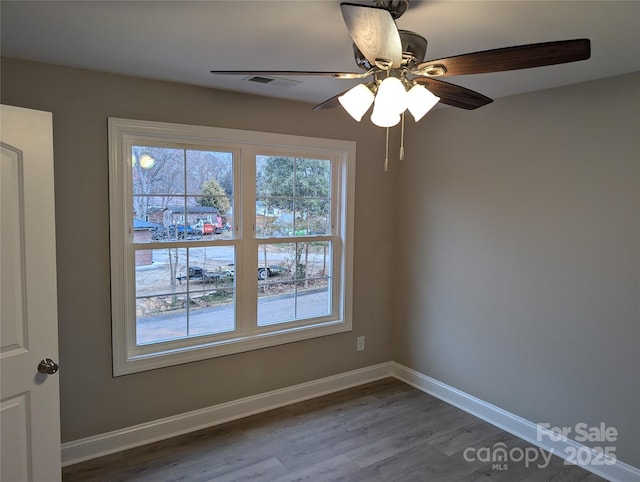 empty room featuring a healthy amount of sunlight, visible vents, baseboards, and wood finished floors