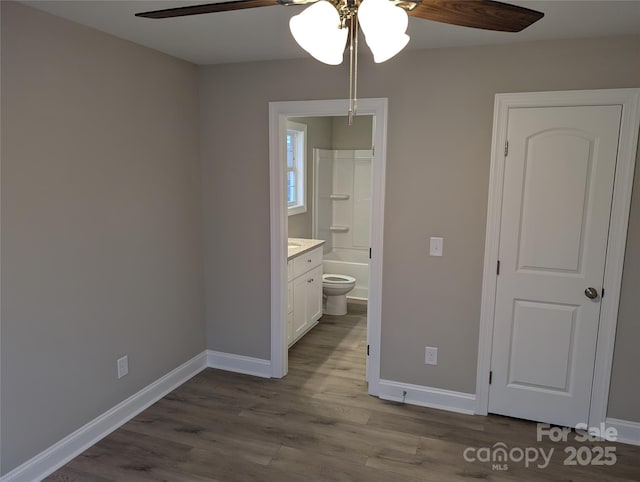 unfurnished bedroom featuring dark wood-style flooring, connected bathroom, baseboards, and ceiling fan