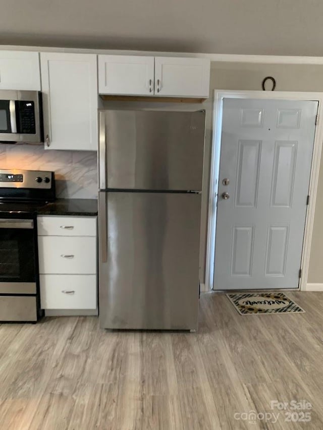 kitchen with dark countertops, light wood-style flooring, appliances with stainless steel finishes, and white cabinets