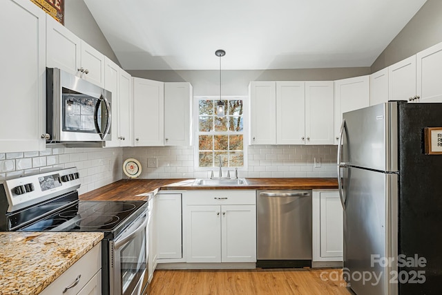 kitchen featuring vaulted ceiling, stainless steel appliances, butcher block countertops, and a sink