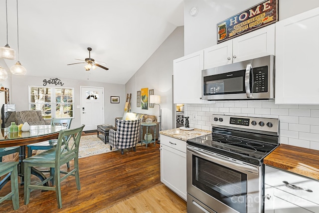 kitchen featuring lofted ceiling, stainless steel appliances, wood finished floors, white cabinets, and decorative backsplash