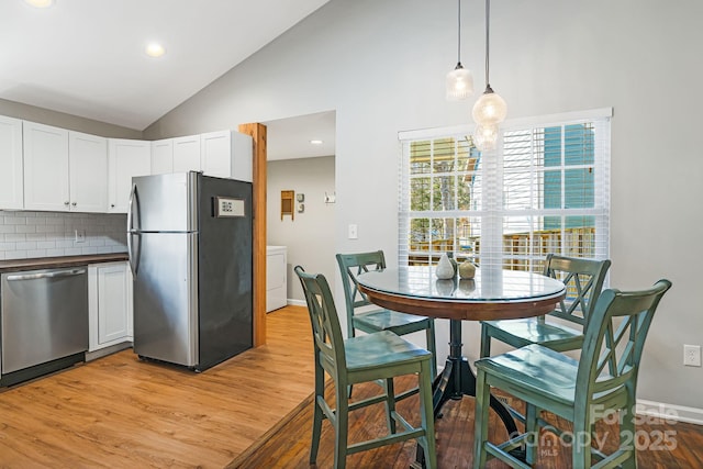 kitchen featuring light wood-style flooring, stainless steel appliances, white cabinetry, hanging light fixtures, and backsplash