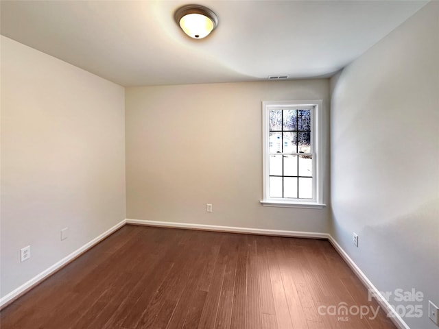 spare room featuring visible vents, baseboards, and dark wood finished floors