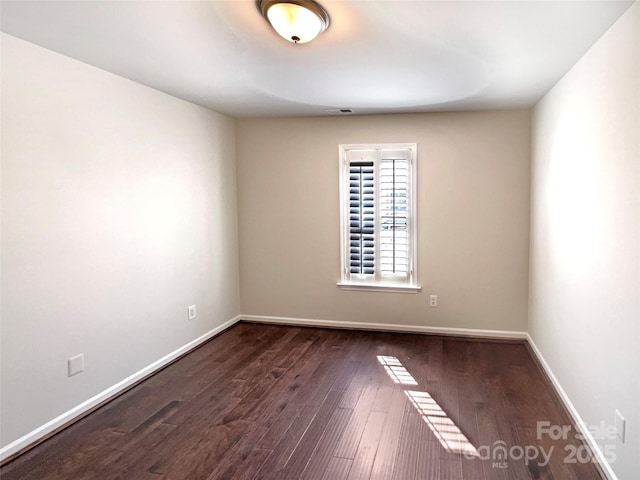 empty room featuring visible vents, baseboards, and dark wood-type flooring