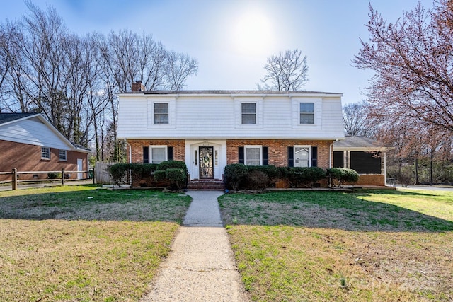 colonial-style house featuring a front yard, brick siding, and fence