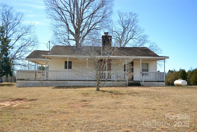 back of property featuring covered porch, a chimney, and a yard