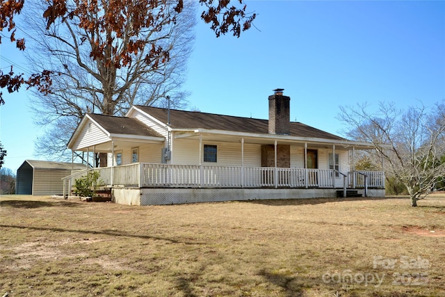 back of house featuring a chimney, a porch, and a lawn