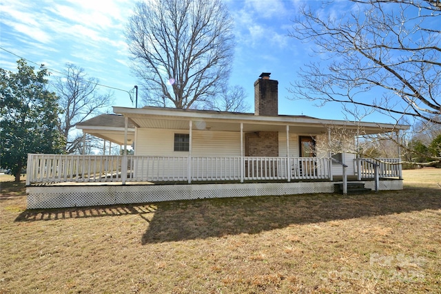 back of house featuring covered porch, a chimney, and a lawn