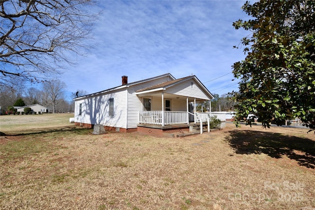 view of front of home with covered porch, a chimney, and a front lawn