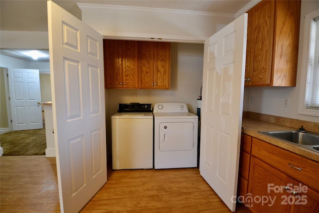 washroom featuring cabinet space, light wood-style flooring, ornamental molding, a sink, and separate washer and dryer