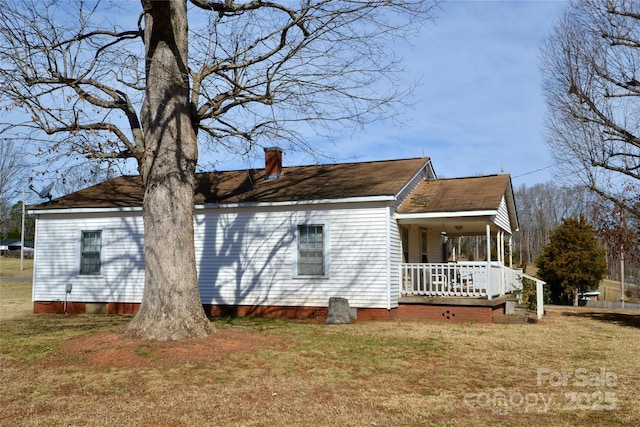 view of side of property with a yard, a porch, and a chimney