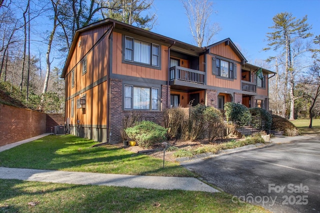 view of front of property with brick siding, a front lawn, fence, and a balcony