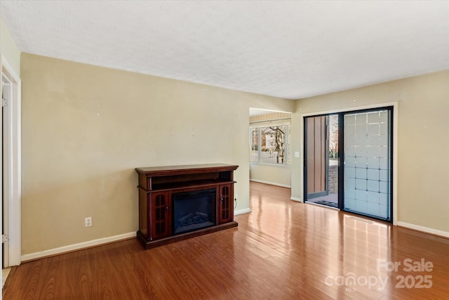 unfurnished living room with a fireplace, a textured ceiling, baseboards, and wood finished floors