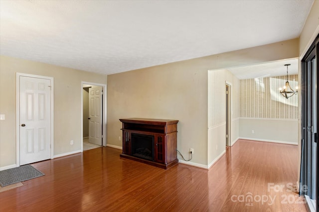 unfurnished living room featuring baseboards, a fireplace, wood finished floors, and a notable chandelier