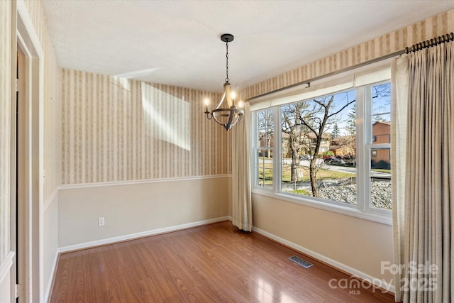 unfurnished dining area with baseboards, plenty of natural light, visible vents, and wood finished floors