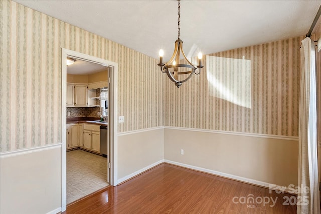 unfurnished dining area featuring wallpapered walls, light wood finished floors, baseboards, a sink, and a notable chandelier