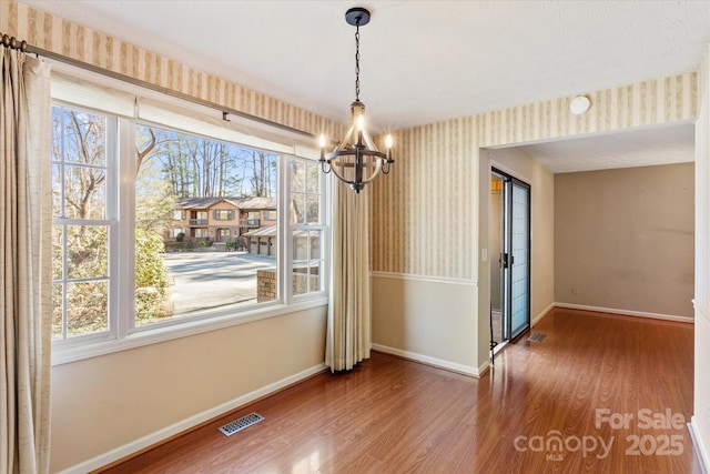 unfurnished dining area featuring visible vents, an inviting chandelier, wood finished floors, baseboards, and wallpapered walls