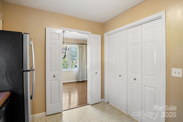 interior space with a textured ceiling, light floors, freestanding refrigerator, and baseboards