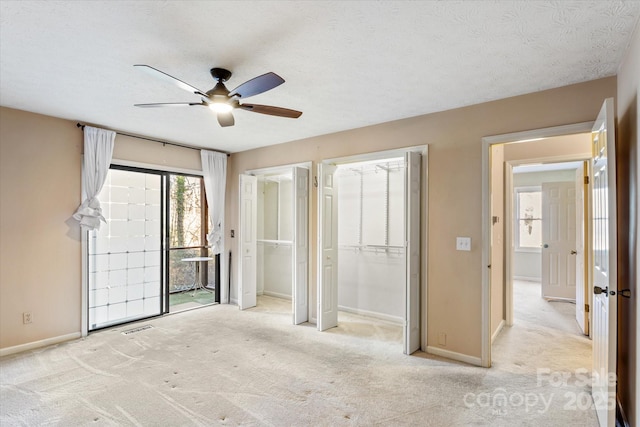 unfurnished bedroom with baseboards, visible vents, a textured ceiling, carpet floors, and two closets