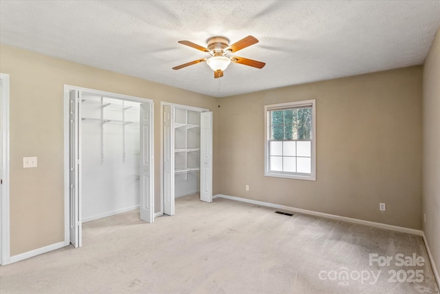 unfurnished bedroom with a textured ceiling, light colored carpet, visible vents, baseboards, and two closets