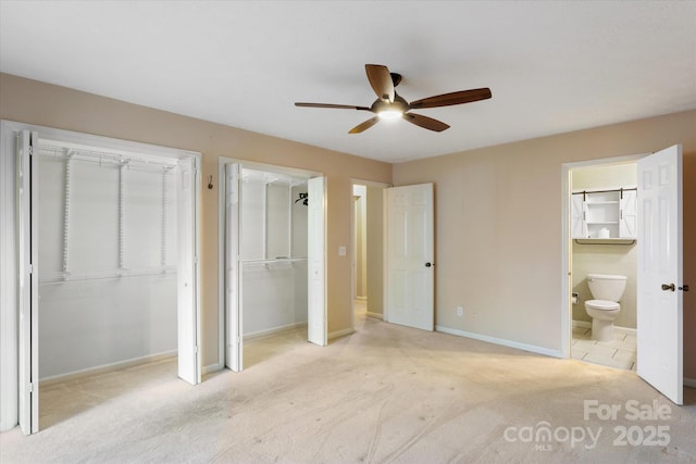 unfurnished bedroom featuring baseboards, carpet flooring, ensuite bath, and two closets