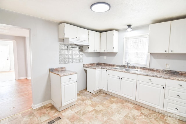 kitchen featuring under cabinet range hood, a sink, visible vents, white cabinets, and baseboards