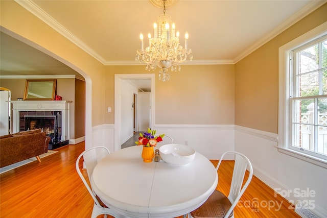 dining room with arched walkways, crown molding, a fireplace, a chandelier, and light wood-type flooring