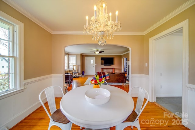 dining area featuring light wood-style floors, arched walkways, crown molding, and plenty of natural light