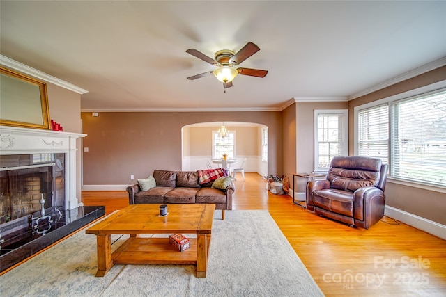 living room featuring light wood-style flooring, a fireplace, arched walkways, and ornamental molding