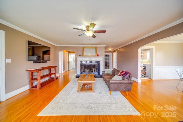 living area featuring light wood-type flooring, arched walkways, a fireplace, and ornamental molding