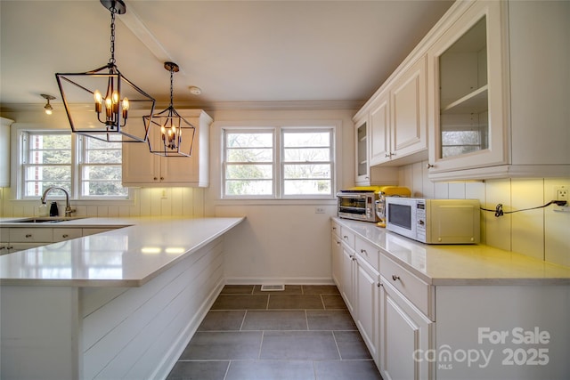 kitchen featuring white microwave, glass insert cabinets, a peninsula, light countertops, and a sink