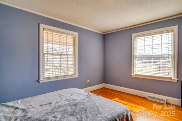 bedroom featuring crown molding, a textured ceiling, visible vents, and wood finished floors