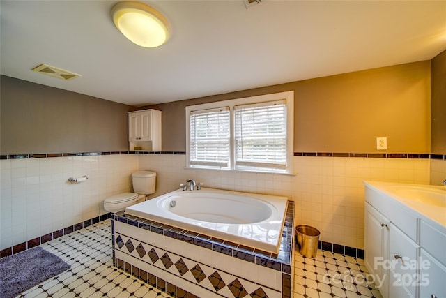 full bathroom with a garden tub, a wainscoted wall, vanity, visible vents, and tile walls