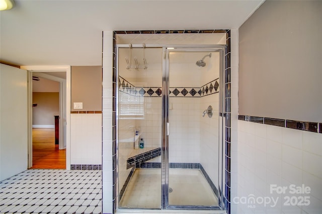 bathroom with a wainscoted wall, a shower stall, and tile walls