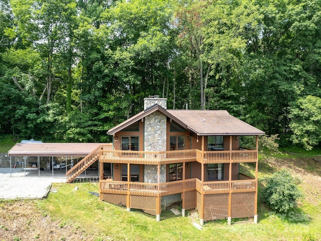 back of house with driveway, a chimney, a deck, a yard, and a carport