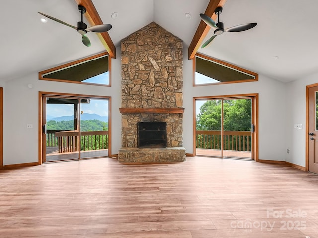 unfurnished living room with a ceiling fan, beamed ceiling, a stone fireplace, and wood finished floors