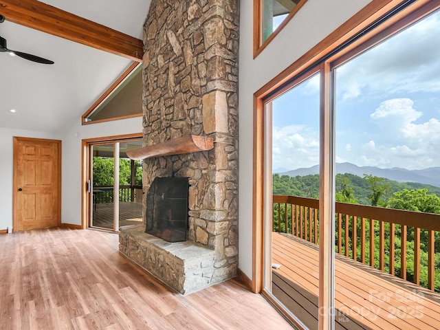 unfurnished living room featuring beam ceiling, a ceiling fan, a mountain view, a stone fireplace, and wood finished floors