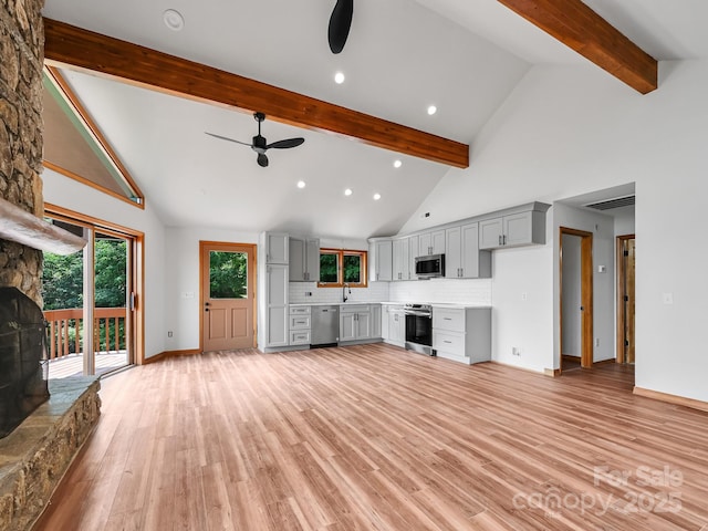 unfurnished living room featuring light wood finished floors, baseboards, a ceiling fan, beamed ceiling, and high vaulted ceiling