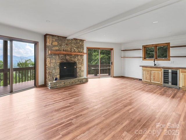 unfurnished living room with wine cooler, a fireplace, light wood-style flooring, and wet bar