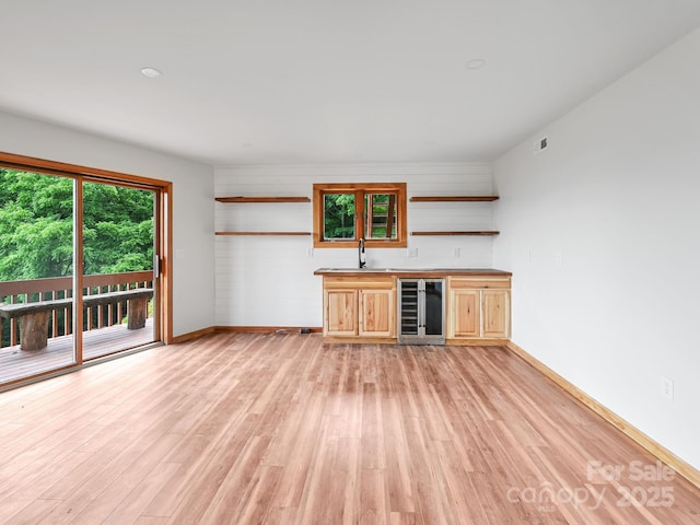 unfurnished living room with beverage cooler, wet bar, light wood-style flooring, and a sink