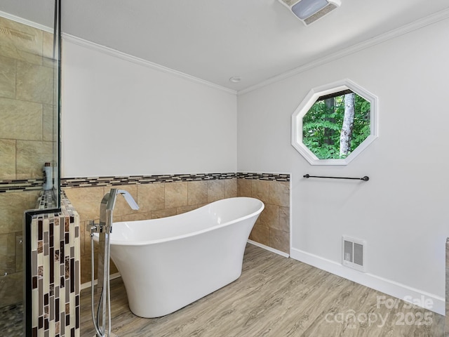 bathroom with visible vents, ornamental molding, wood finished floors, a freestanding tub, and tiled shower