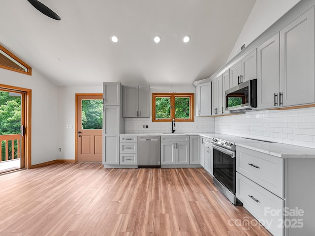 kitchen with decorative backsplash, lofted ceiling, appliances with stainless steel finishes, gray cabinetry, and light wood-style floors