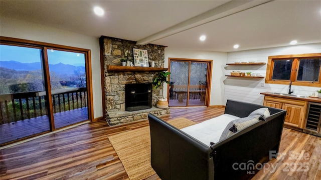 living room featuring wine cooler, beamed ceiling, a fireplace, and light wood-style flooring