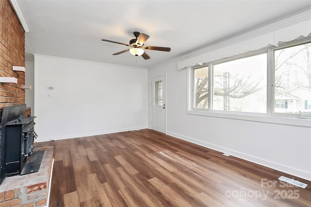 unfurnished living room with wood finished floors, a ceiling fan, visible vents, a wood stove, and crown molding