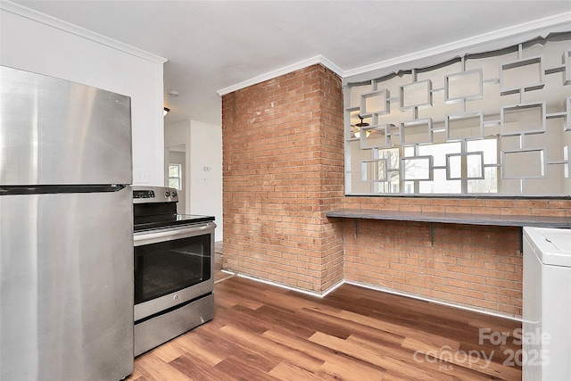 kitchen featuring stainless steel appliances, ornamental molding, brick wall, and wood finished floors