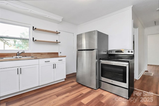 kitchen featuring stainless steel appliances, a sink, light wood-style floors, white cabinets, and crown molding