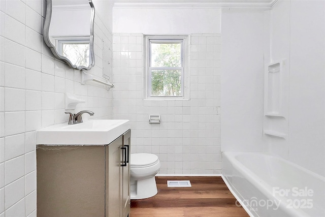 full bath featuring toilet, wood finished floors, visible vents, vanity, and tile walls