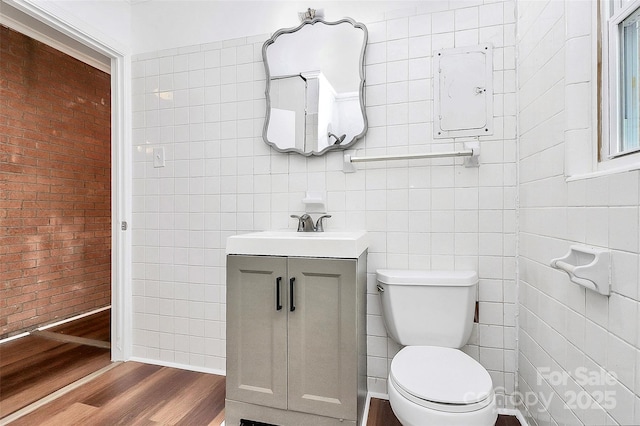 half bathroom with tile walls, toilet, vanity, brick wall, and wood finished floors