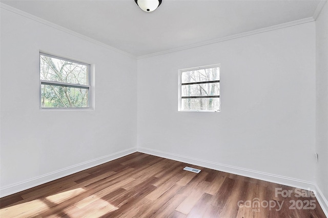 empty room featuring dark wood-style floors, visible vents, crown molding, and baseboards