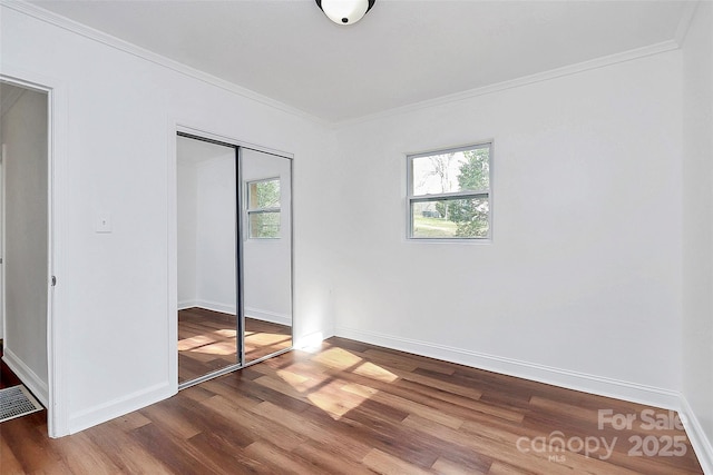 unfurnished bedroom featuring ornamental molding, a closet, multiple windows, and wood finished floors